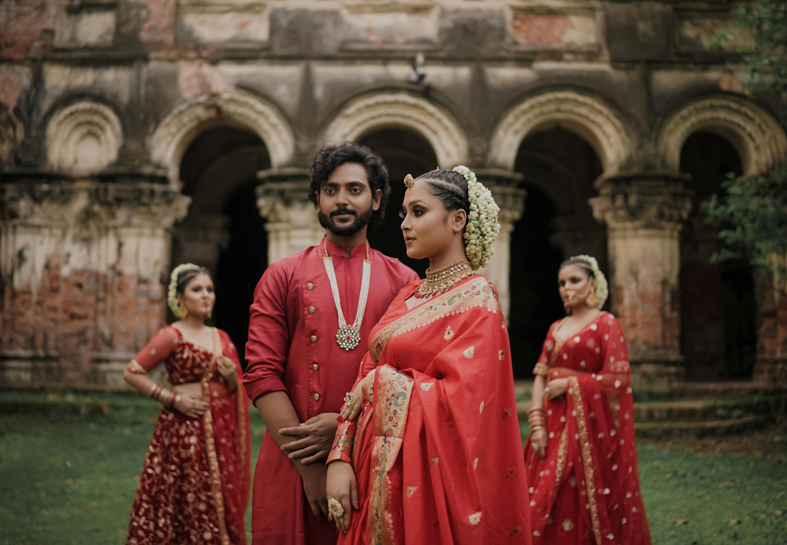 Group in traditional Indian wedding attire in front of historic architecture.